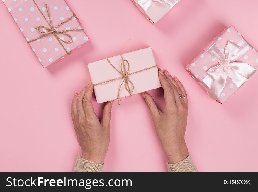 Womans hands holding gift or present box on pink pastel table top view. Flat lay composition for birthday or New Year