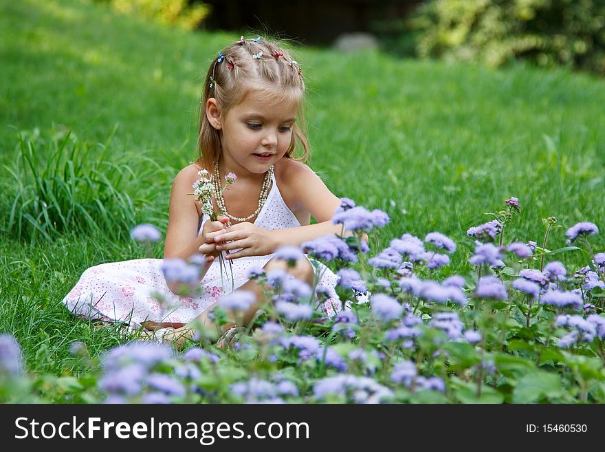 A little girl sitting in the meadow with flowers