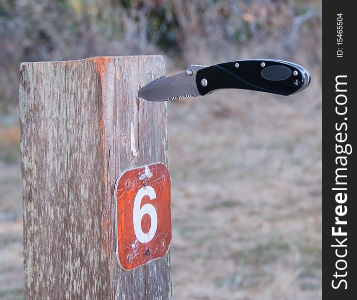 Folding knife stuck in camp site sign post. Folding knife stuck in camp site sign post