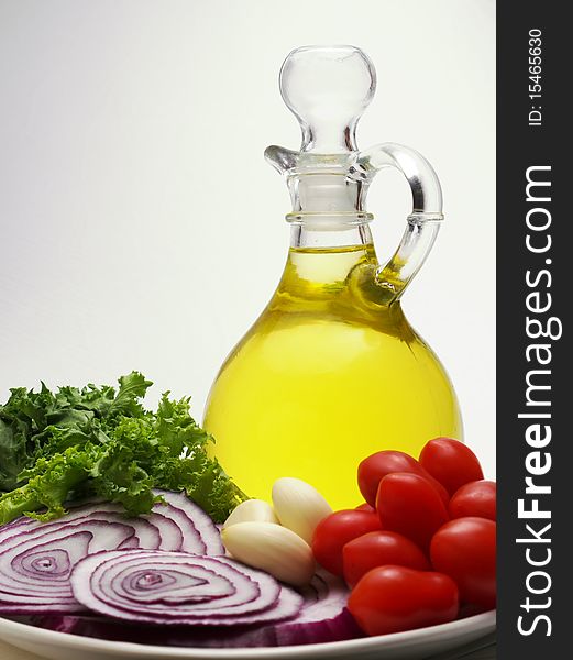 Decanter of olive oil with tomatoes, garlic, sliced red onions, greens, on white background, copyspace. Decanter of olive oil with tomatoes, garlic, sliced red onions, greens, on white background, copyspace