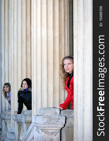 Three girls behind the columns look afar. Three girls behind the columns look afar