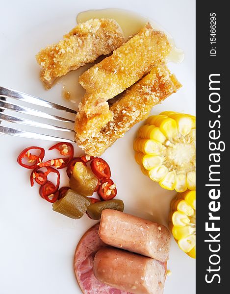 Various food for breakfast, with fork in white dish, corn, sausage, ham, fried meat and some pickle. Various food for breakfast, with fork in white dish, corn, sausage, ham, fried meat and some pickle.