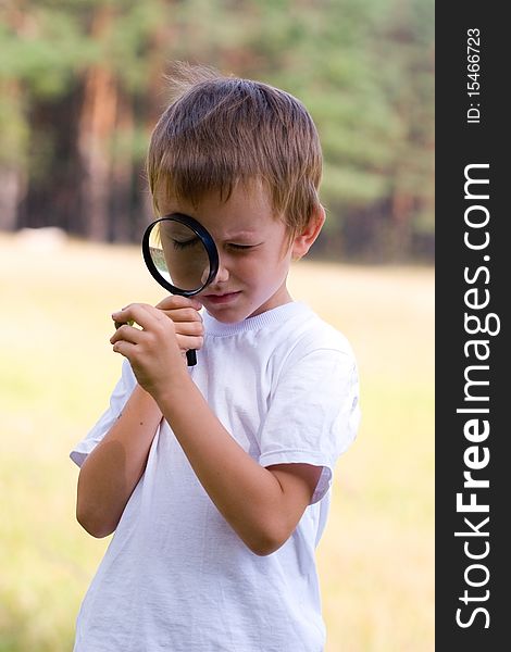 Happy boy with a magnifying glass outdoors on a summer day