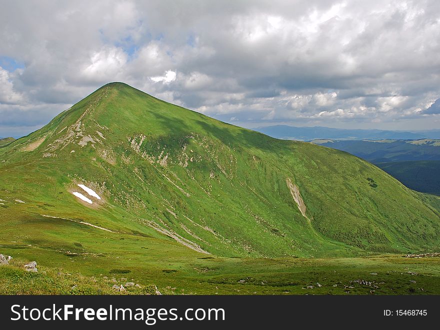 Mountain top in a summer landscape under dense clouds with green slopes. Mountain top in a summer landscape under dense clouds with green slopes.