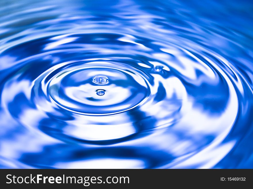 Clean blue drop of water splashing in clear water. Abstract blue background