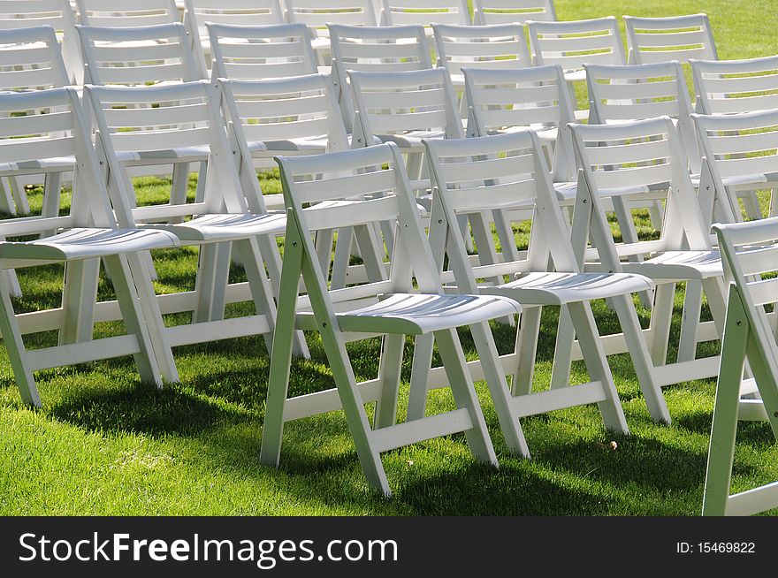 A bunch of white chairs in rows on green grass. A bunch of white chairs in rows on green grass.