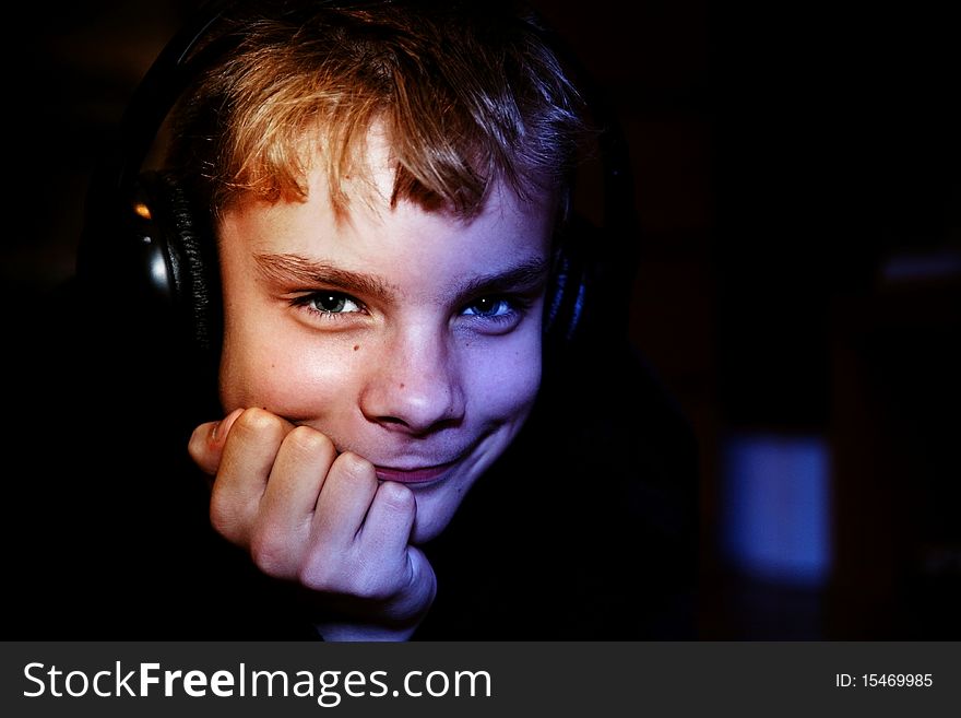 Portrait of the cute teenager with headphones on a dark background close up