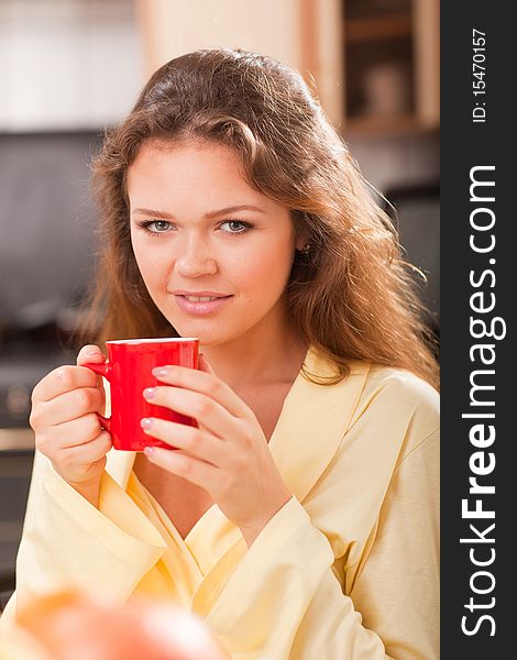 Attractive young adult with red cup of tea in the kitchen. Attractive young adult with red cup of tea in the kitchen