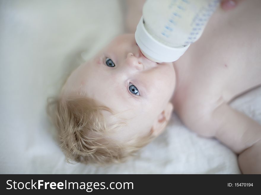 Baby drinking a bottle of milk on the bed