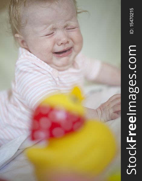 Crying baby on the bed - little toy duck in foreground