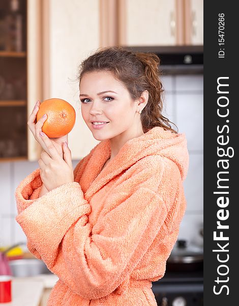 Woman with healthy smile holding orange in the kitchen wearing bathrobe. Woman with healthy smile holding orange in the kitchen wearing bathrobe