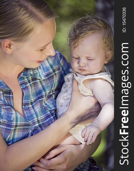 Happy mother holding unhappy baby in the hands - outdoors. Happy mother holding unhappy baby in the hands - outdoors