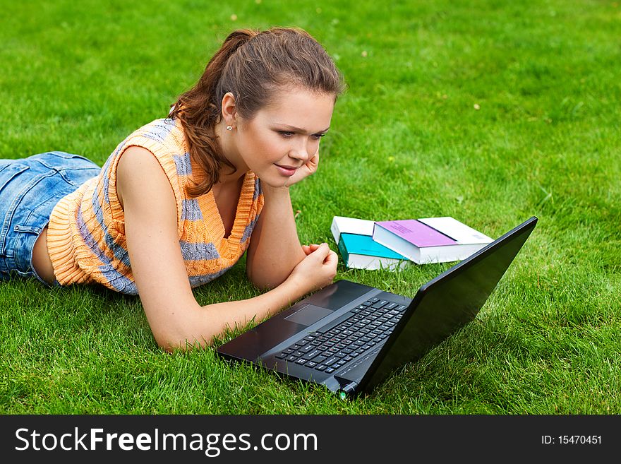 Pretty young adult with laptop lying on green grass. Pretty young adult with laptop lying on green grass