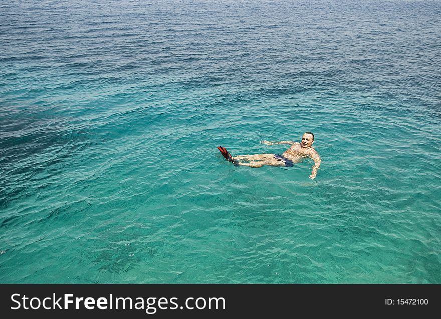 Color photo of a happy smiling man in his forties wearing red flippers and floating in the blue turquoise water of the ionian sea in Greece. Color photo of a happy smiling man in his forties wearing red flippers and floating in the blue turquoise water of the ionian sea in Greece.