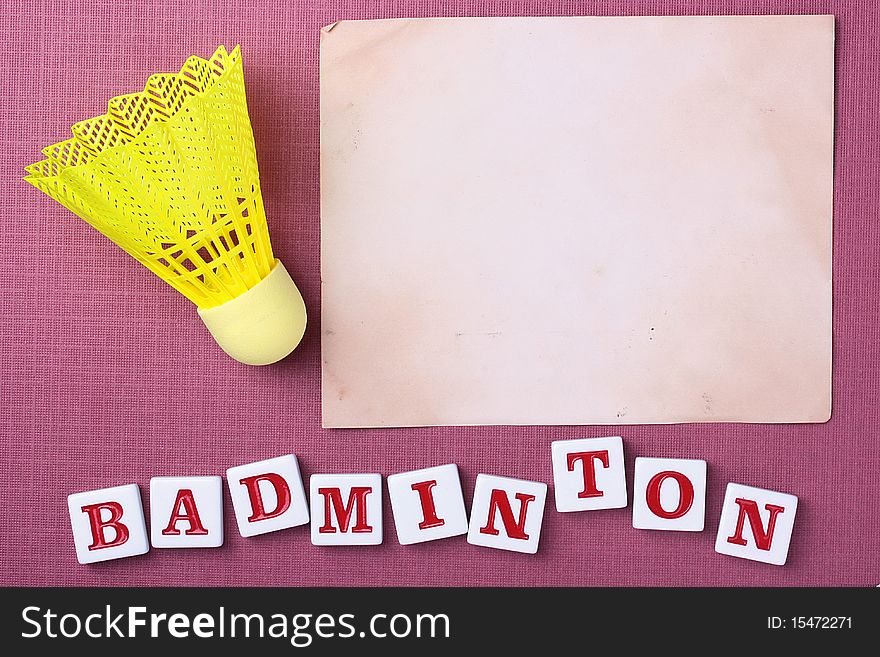 A yellow synthetic badminton shuttlecock next to a piece of paper. Add your text to the paper.