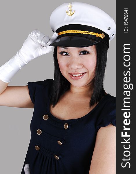 A young pretty Asian woman with cloves with a sailors cap, navy blue shirt, saluting over light gray background. A young pretty Asian woman with cloves with a sailors cap, navy blue shirt, saluting over light gray background.