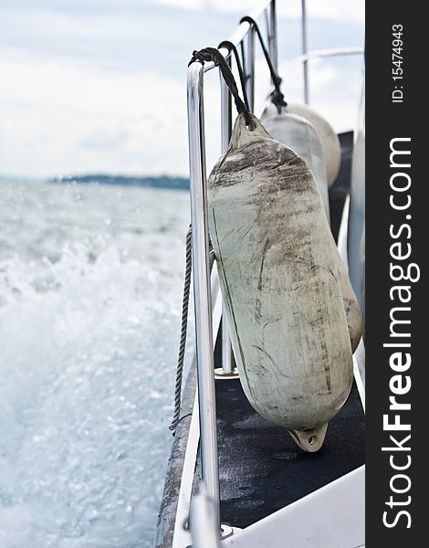 Some boat bumpers tied to a railing on the side of a boat moving fast through the water. Some boat bumpers tied to a railing on the side of a boat moving fast through the water.