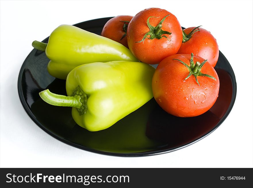 Fresh tomatoes and peppers washed and placed in a black ceramic plate isolated on white background. Fresh tomatoes and peppers washed and placed in a black ceramic plate isolated on white background