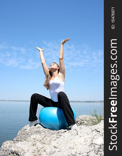 Young woman stretching to the sun, sitting on the blue fitness ball