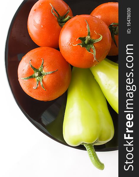 Tomatoes and peppers washed and placed in a black ceramic plate isolated on white background top view