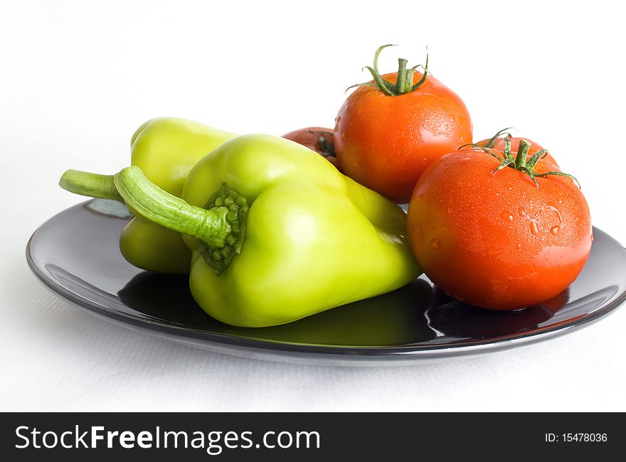Fresh tomatoes and peppers washed and placed in a black ceramic plate isolated on white background. Fresh tomatoes and peppers washed and placed in a black ceramic plate isolated on white background