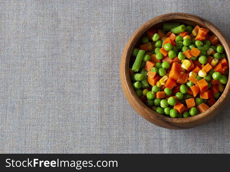 Mixed vegetables, with carrot, beans, peas and sweet corn,  in a wooden bowl.  On a grey textured cotton tablecloth