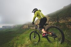 Aged Male Athlete In Helmet And Mask Rides A Mountain Bike On A Grassy Slope Against The Background Of Plateau Rocks And Royalty Free Stock Photos
