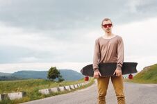 A Stylish Young Man Standing Along A Winding Mountain Road With A Skate Or Longboard In His Hands The Evening After Royalty Free Stock Photo