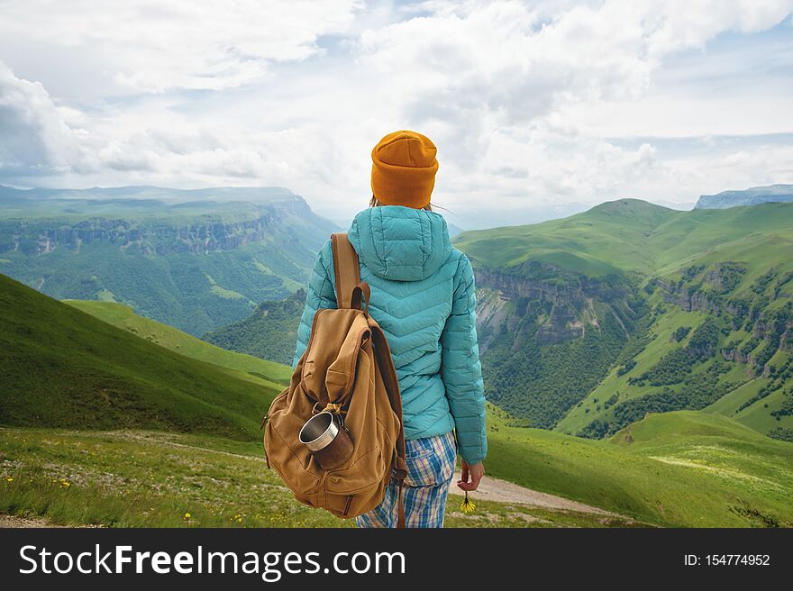 The view from the back of a tourist girl with a backpack is standing and looking at the mountain green valleys and