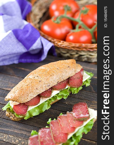 Sandwich with dry meat, lettuce, and cheese on dark wooden table top