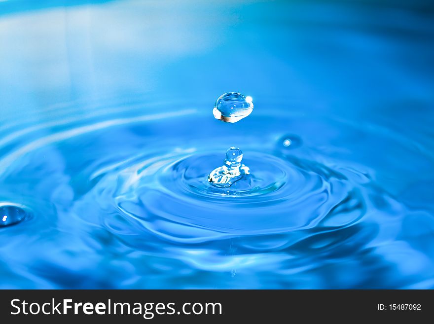 Clean blue drop of water splashing in clear water. Abstract blue background