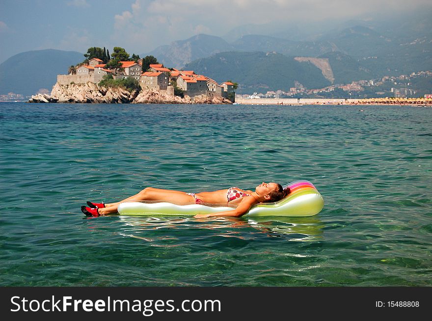 A girl sunbathing on a mattress in Adriatic waters against Sveti Stefan in Montenegro