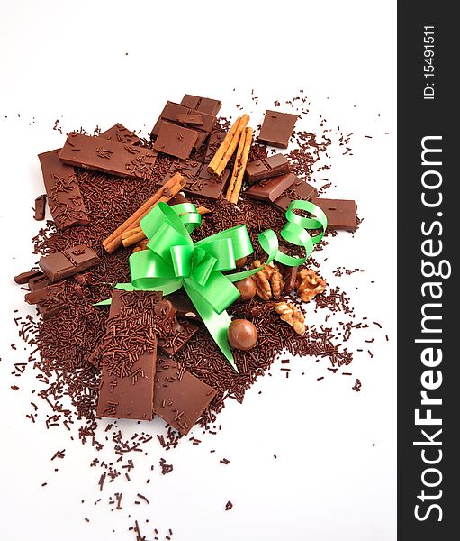 The broken chocolate, chocolate shaving cinnamon and nuts and a green bow on a white background. The broken chocolate, chocolate shaving cinnamon and nuts and a green bow on a white background