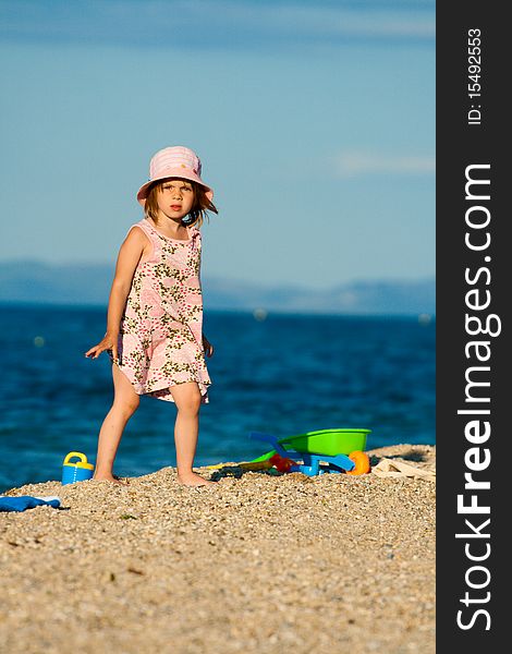 Little beautiful girl goes on the beach against the blue of the sea among his toys. Little beautiful girl goes on the beach against the blue of the sea among his toys.