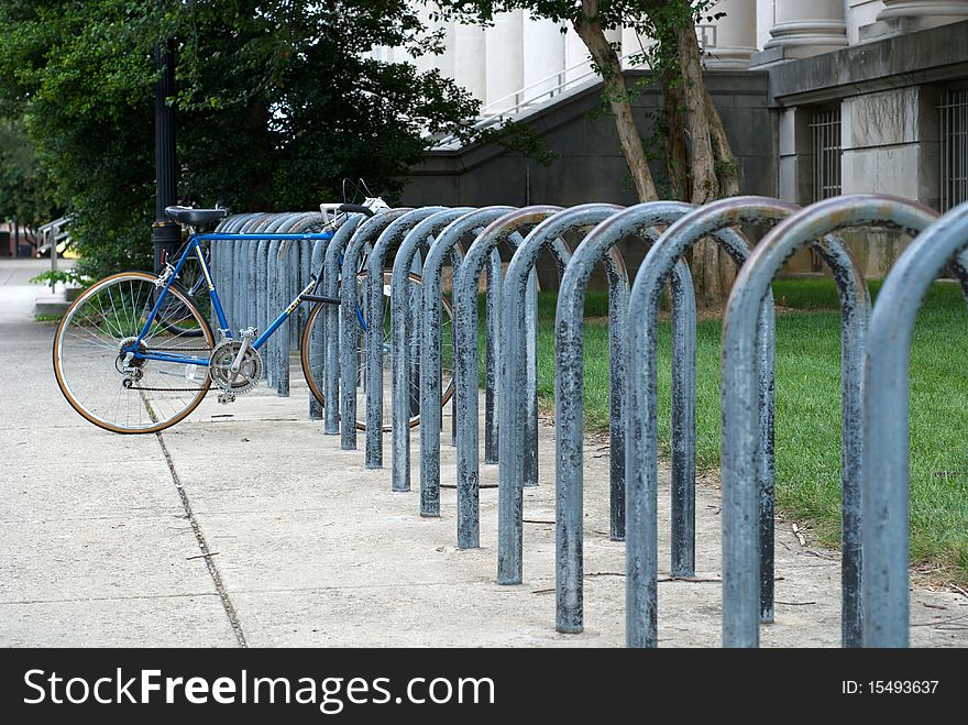 A lone bicycle attached to repeating metal loops for a bicycle rack.