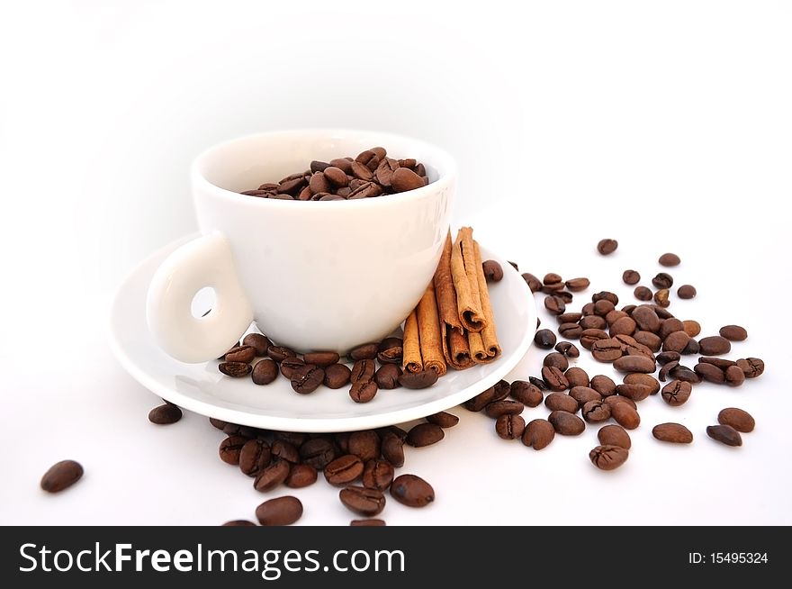 White cup of coffee, with coffee grains inside and cinnamon on a saucer on a white background. White cup of coffee, with coffee grains inside and cinnamon on a saucer on a white background