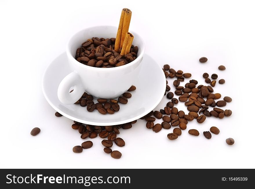 White cup of coffee, with coffee grains inside and cinnamon on a saucer on a white background. White cup of coffee, with coffee grains inside and cinnamon on a saucer on a white background