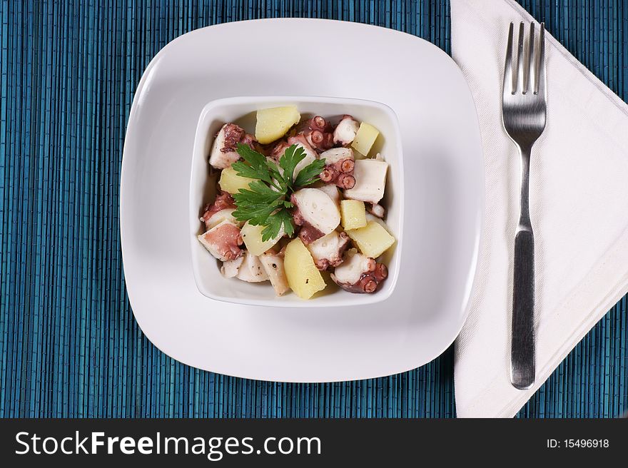 Boiled octopus with potatoes served in a white dish. Laid table.