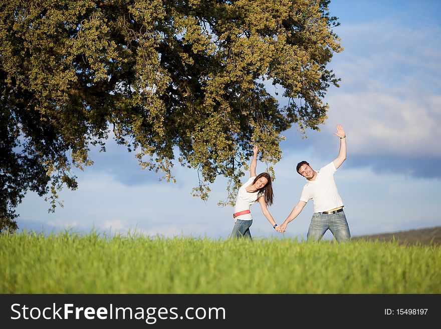 Young beautiful couple hand by hand doing some sport movements under a tree. Young beautiful couple hand by hand doing some sport movements under a tree.