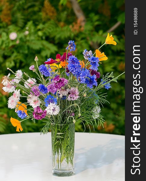 Years bouquet of dark blue cornflowers on a background of a green bush on a white table