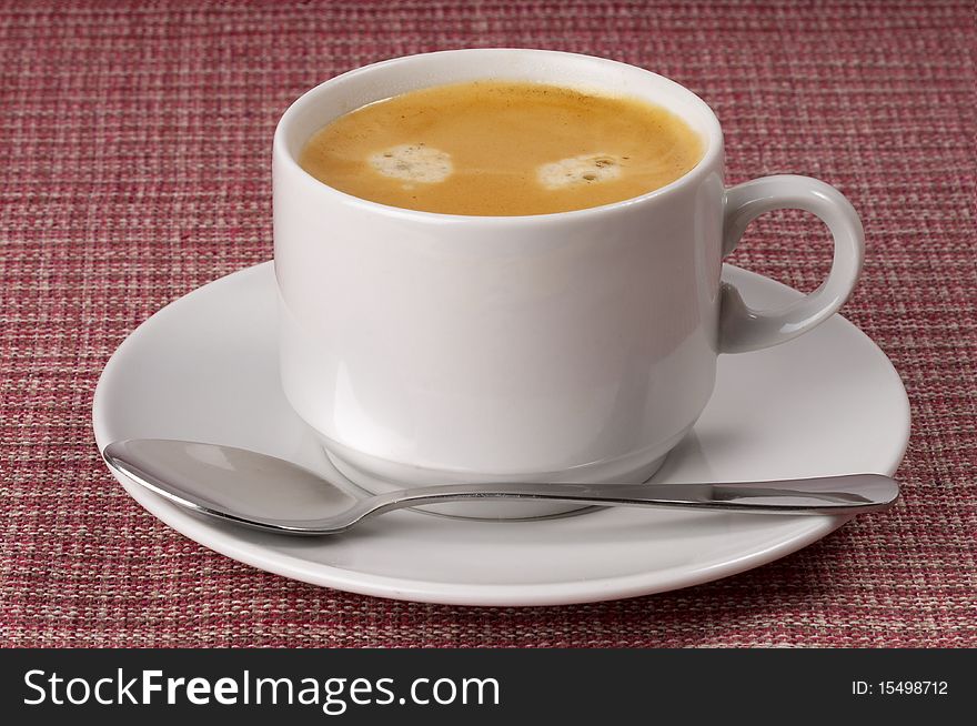 Little white espresso coffee cup on a white saucer over checked table-cloth background