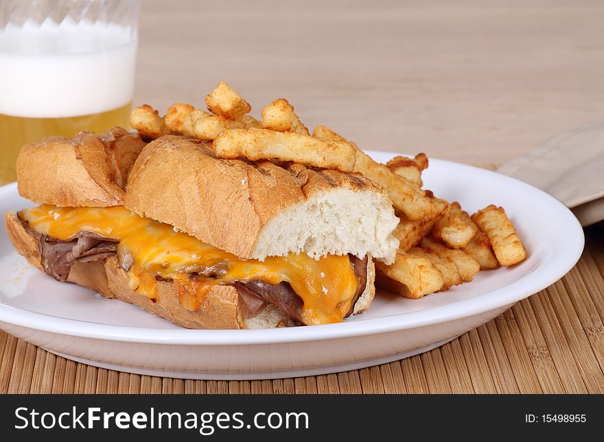 Roast beef sandwich covered with melted cheese along with french fries and a beer. Roast beef sandwich covered with melted cheese along with french fries and a beer