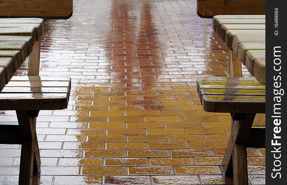 Outdoor cafe on a rainy day. Reflection of people on wet sidewalk, rain drops fall on benches