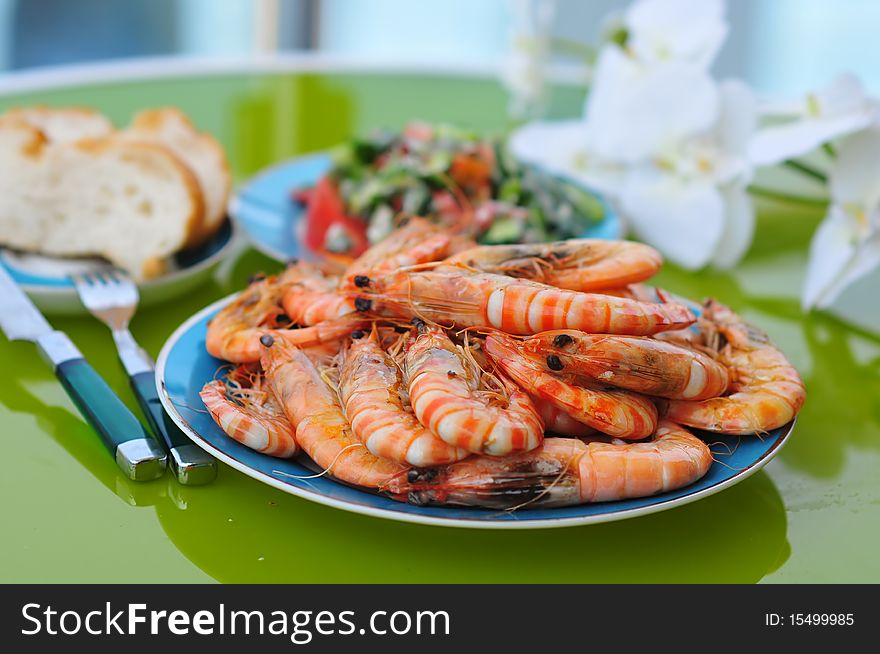 Dish served with a lot of fried tiger prawns with a knife and fork, bread and green salad on the table with flowers. Dish served with a lot of fried tiger prawns with a knife and fork, bread and green salad on the table with flowers