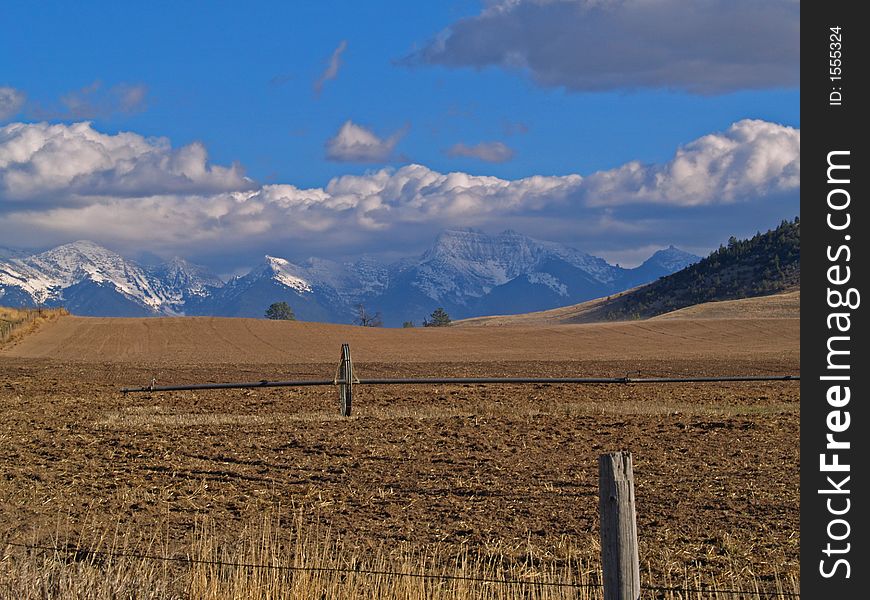 This image of the agricultural field, fence, irrigation pipe and wheel, and snowcapped mountains was taken in western MT. This image of the agricultural field, fence, irrigation pipe and wheel, and snowcapped mountains was taken in western MT.