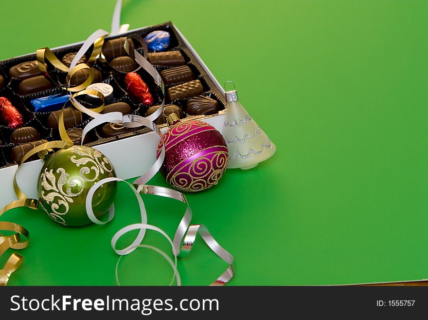 A box of fine chocolate on green background, christmas balls and decorations. A box of fine chocolate on green background, christmas balls and decorations