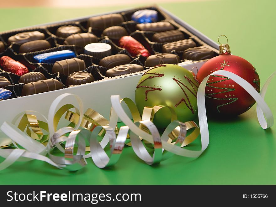 A box of fine chocolate on green background, christmas balls and decorations. A box of fine chocolate on green background, christmas balls and decorations