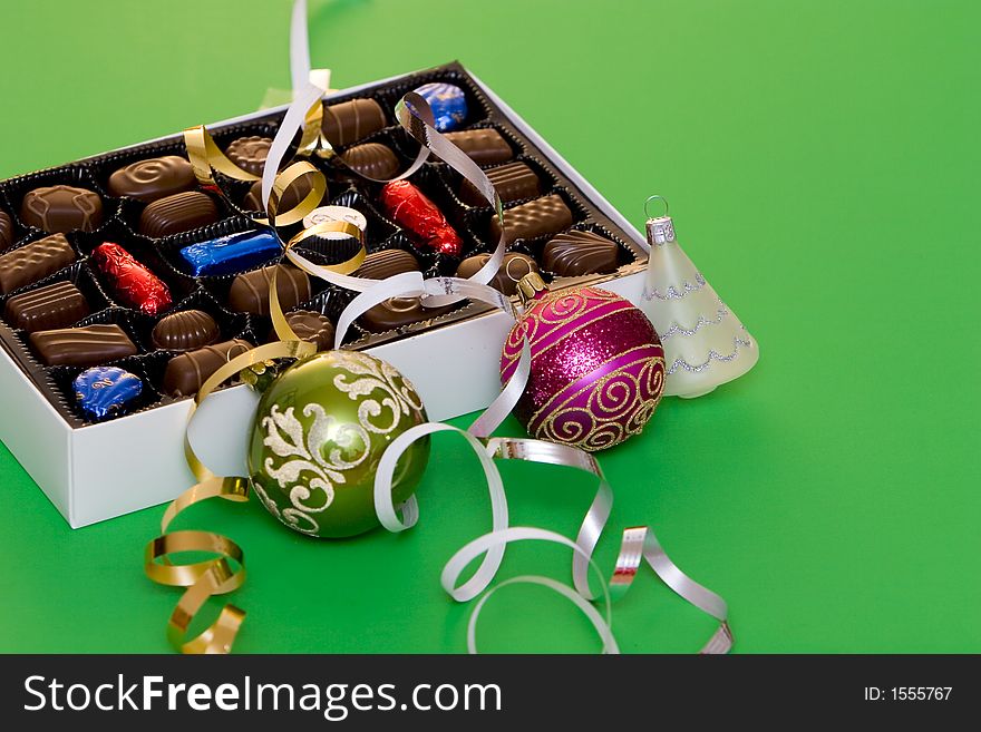 A box of fine chocolate on green background, christmas balls and decorations. A box of fine chocolate on green background, christmas balls and decorations