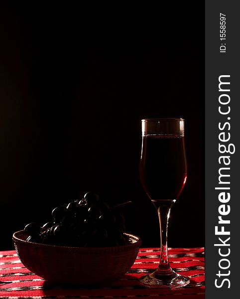 Cup with red wine and red grapes in straw basket, black background. Cup with red wine and red grapes in straw basket, black background