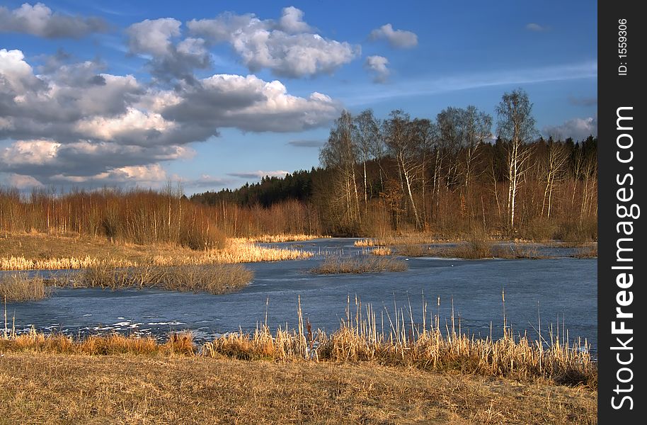 March landscape with leafless trees and frozen lake